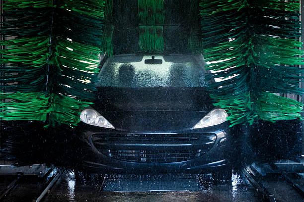 Front view of a black car being washed in an automatic car wash with green rotating brushes