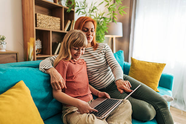 istock Mother and daughter using laptop together on sofa at home 2209543561