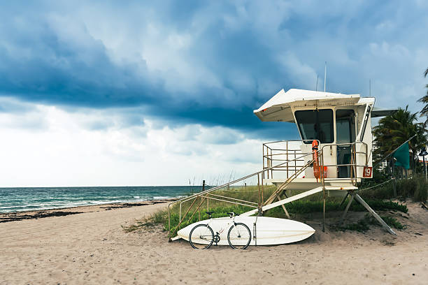 This evocative photograph portrays a lifeguard tower standing as a solitary guardian against an ominous, storm-laden sky. Positioned on a serene, sandy beach, the tower is marked with \