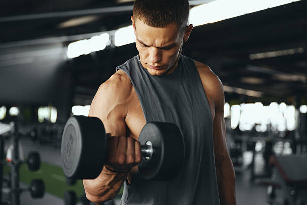 istock Young handsome man bodybuilder weightlifter training biceps with dumbbells while looking at muscles 2209546106