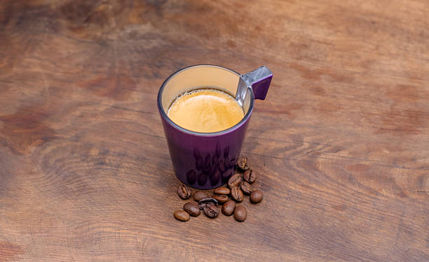 Purple coffee cup with espresso and beans on wooden table.