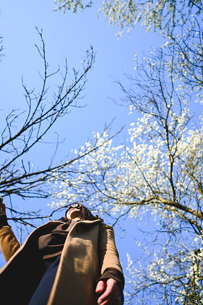 istock Young woman looking up at blooming trees in spring 2209547399