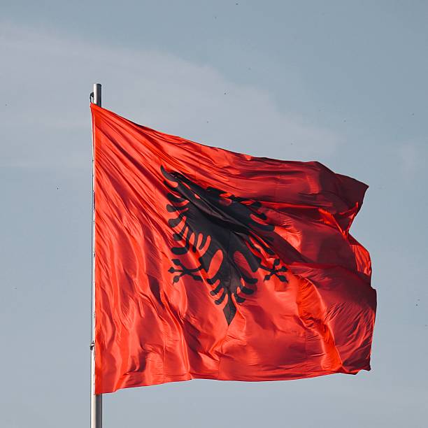 The national flag of Albania waves boldly against a clear blue sky. Its striking red background is adorned with a black double-headed eagle.