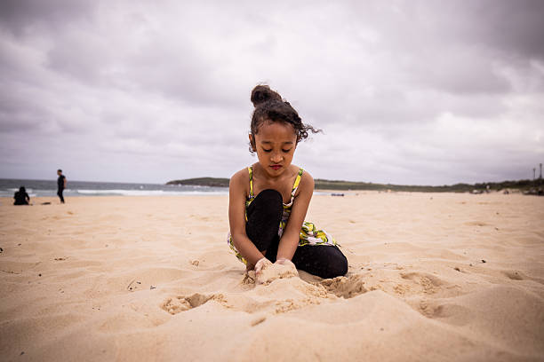 Pacific Islander little girl in playing in sand by the sea on the beach.