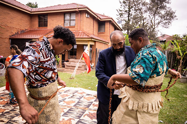 Pacific Islanders man preparing his teenage sons for a traditional dance, tying belts and adjusting accessories of traditional clothing.