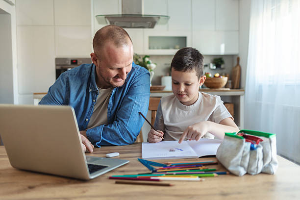 istock Shot of a young father using a laptop while his son does homework at home. 2209560677
