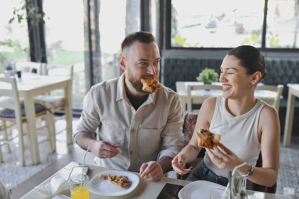 istock Female Laughing at Boyfriend Acting Goofy While Biting Into Pizza Slice 2209562151