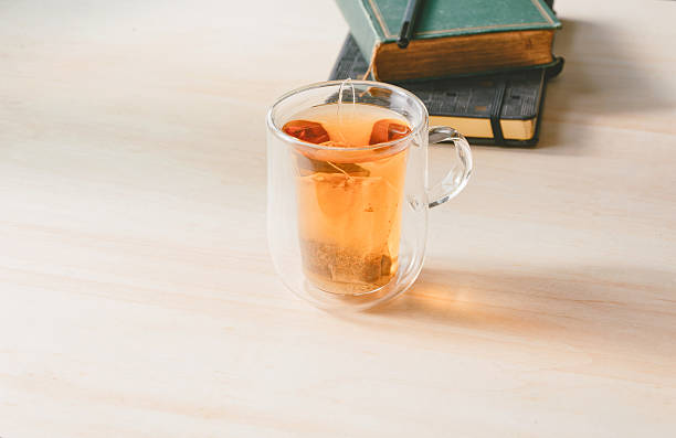 Tea in glass mug with journal in background on wooden table, part of mental health routine  - journal for therapy session - copy space for text, concepts and ideas, healthy lifestyle