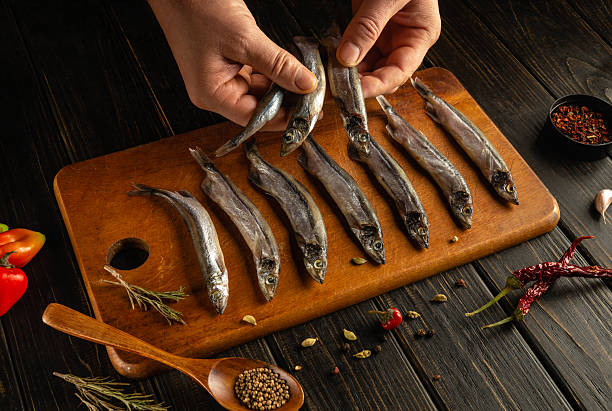 istock Hands hold several fresh fish while arranging them on a wooden cutting board. Various herbs and spices accompany the fish along with vegetables, creating a vibrant culinary display 2209579422