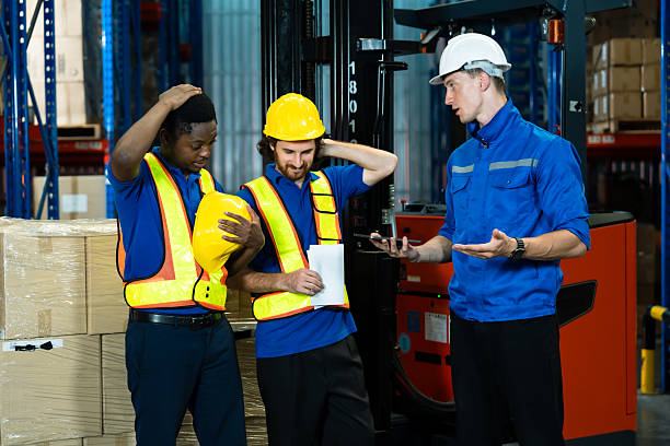 istock Three adult male warehouse workers discussing logistics issue one wearing white helmet appears giving instruction while other two look concerned showing team communication and problem-solving. 2209579498