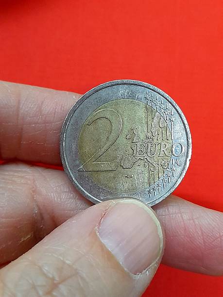 istock 2 euro coin in hand with red background 2209580741