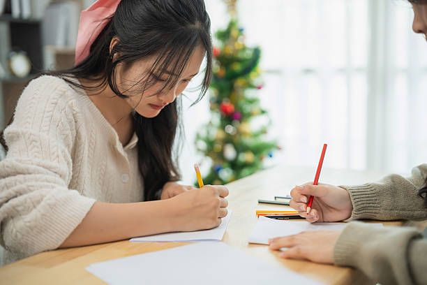 istock Young woman writing in a notebook with colored pencils while sitting at a table, festive decorations in the background, creative atmosphere 2209582050