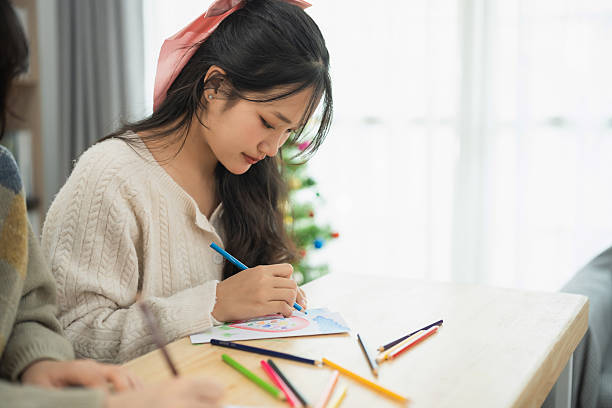istock Young Woman Engaged in Creative Drawing Activity with Colored Pencils in a Cozy Indoor Setting During Winter Season 2209582102
