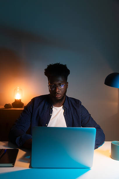 istock Focused young man working late on laptop in dimly lit room 2209583608
