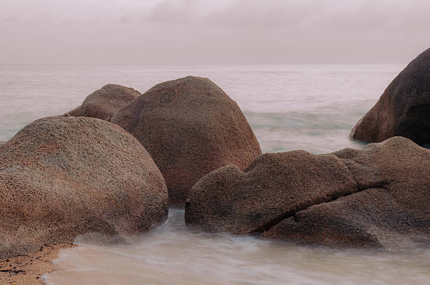 Long exposure of smooth ocean waves washing over granite boulders on a tropical beach at dawn, Ko Samui, Thailand