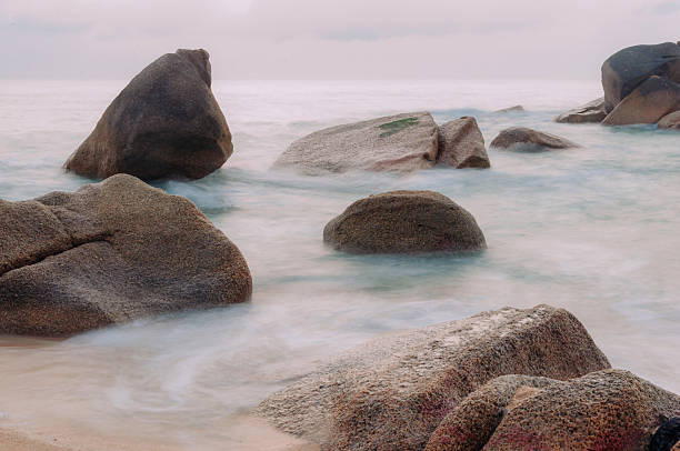 Long exposure shot of smooth waves washing over rocks on a sandy beach at dawn, Ko Samui, Thailand