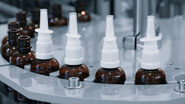istock medicine bottles, each with a white cap, are lined up on a manufacturing packaging line. The bottles are brown and white and they appear to be in a row. 2209601474