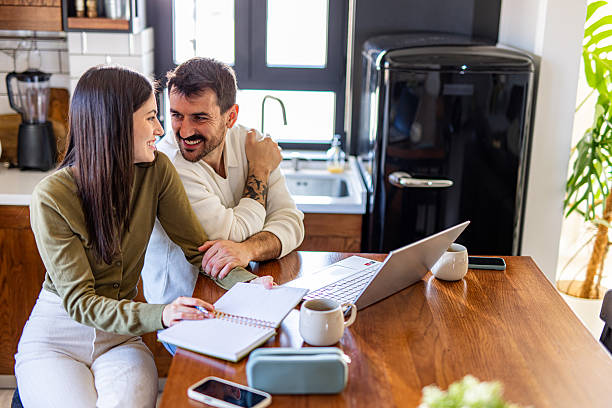 istock Happy couple working from home using laptop and taking notes in kitchen 2209602370