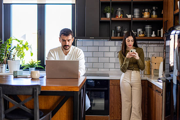 istock Couple Working From Home, Man Using Laptop and Woman Using Smartphone in Kitchen 2209603373