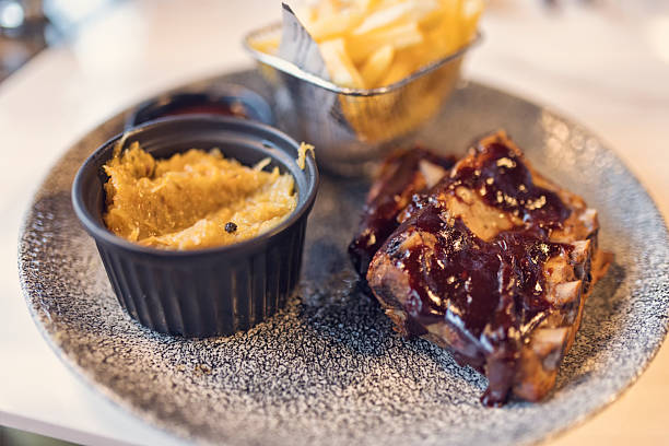 Succulent pork ribs with barbecue sauce, potato and coleslaw on white plate in daylight at restaurant