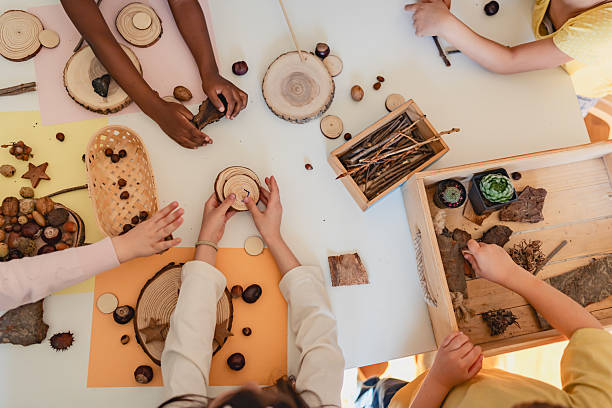 Multicultural group of children engaged in a nature-inspired arts and crafts activity using natural materials at a preschool table.