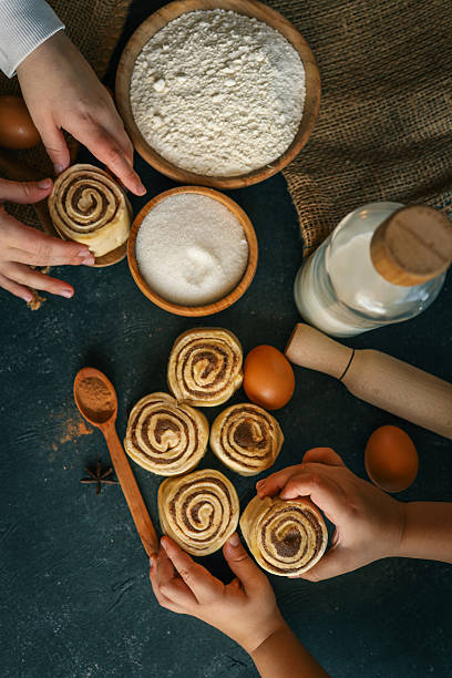 istock Children rolling cinnamon buns on a dark surface with flour, sugar, eggs, and milk, capturing a cozy baking scene, perfect for family cooking themes 2209616082