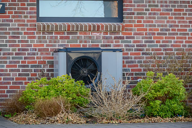 istock Heat pump system installed in front of a residential brick wall, surrounded by early spring vegetation. Air-source heat pump mounted on brick wall with garden landscaping. 2209617304