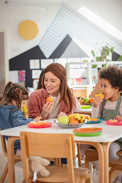 istock A diverse group of preschool children sits around a table eating healthy snacks while a teacher engages with them, promoting nutrition, inclusion, and social interaction in early education. 2209617478