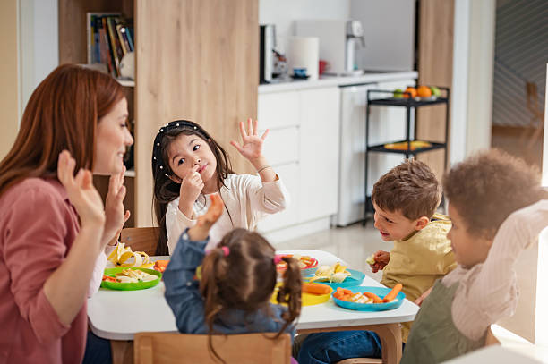 istock A diverse group of preschool children sits around a table eating healthy snacks while a teacher engages with them, promoting nutrition, inclusion, and social interaction in early education. 2209617554