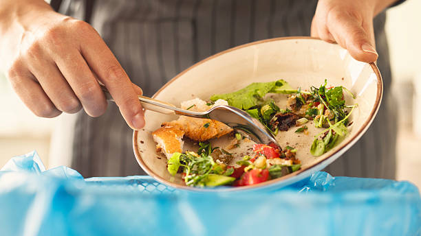 istock Woman scraping leftover food from plate into trash bin in kitchen 2209621341