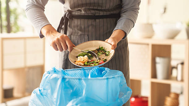 istock Woman scraping leftover food from plate into trash bin in kitchen 2209621460
