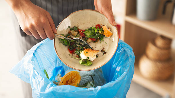 istock Woman scraping leftover food from plate into trash bin in kitchen 2209621461