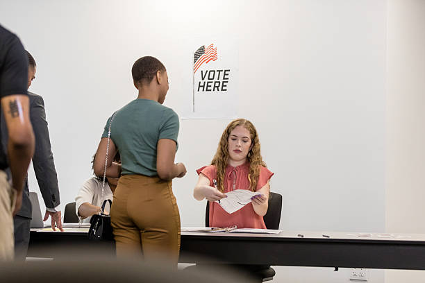Election day, young woman helps voters register.  Casual attire, indoors.