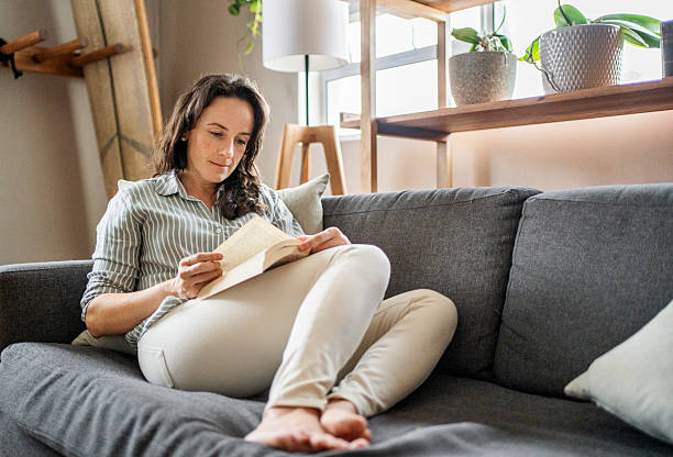 istock Woman relaxing on sofa reading a book in modern apartment 2209625159