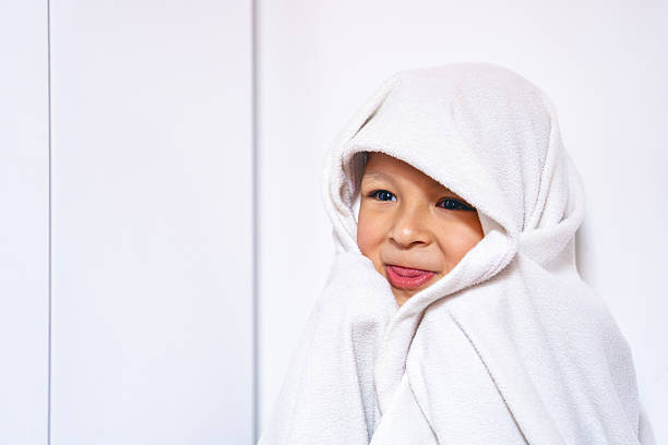 A young boy covers himself with a white blanket while smiling and playing, creating an imaginary hideout. A spontaneous moment capturing the simple, authentic joy of childhood.