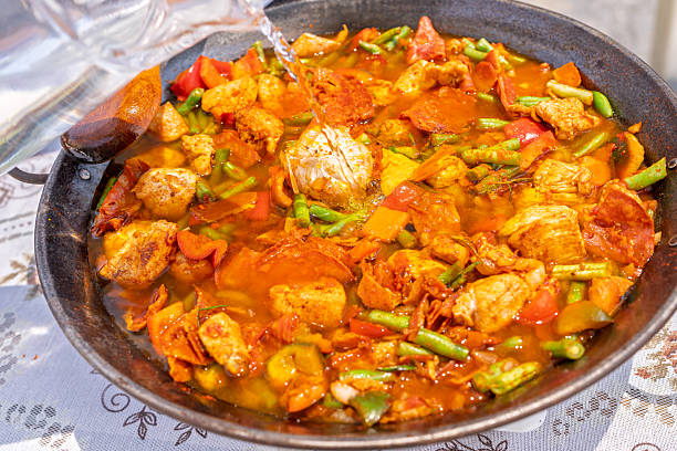 Cook adding water to a paella with chicken, vegetables and chorizo, during its preparation