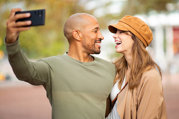 istock happy couple standing outdoors taking selfie and looking at each other 2209636424