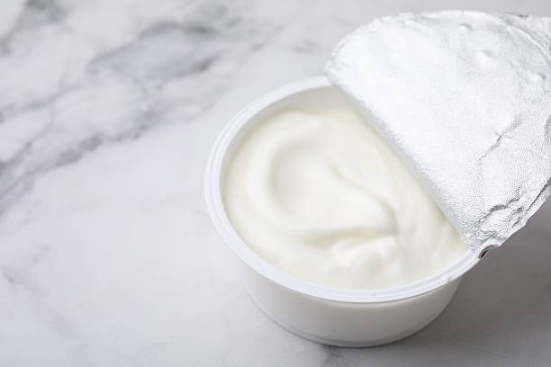 istock Delicious natural yogurt in plastic cup on white marble table, closeup. Space for text 2209639721