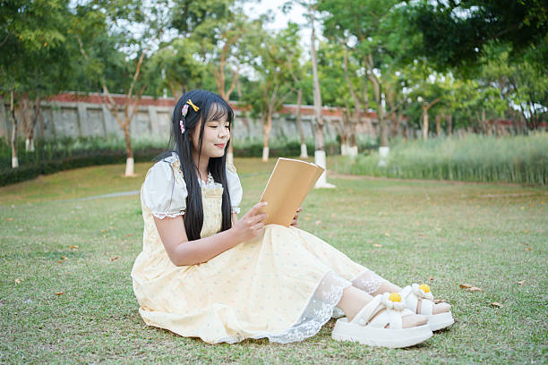 Young Asian woman sitting on the grass in the park and reading a book