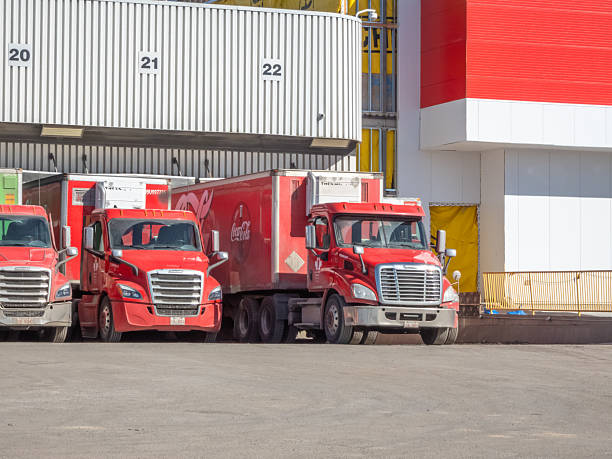 Calgary, Alberta, Canada. Apr 10, 2025. Several red Coca-Cola delivery trucks are parked in a row at loading docks.