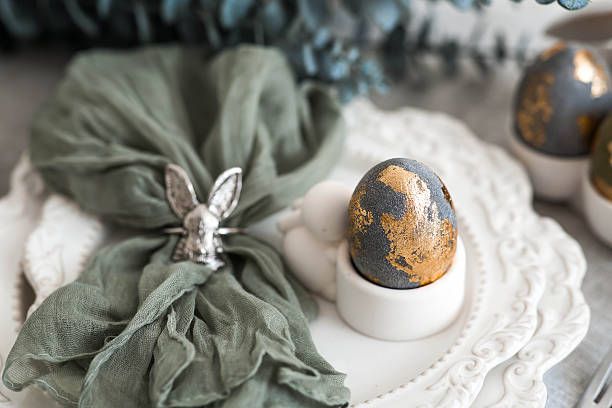 istock The banner. Table setting. A plate with a rabbit and a napkin, Easter eggs with gilding and a branch of eucalyptus on a linen tablecloth. The concept of a bright Easter holiday. 2209670011