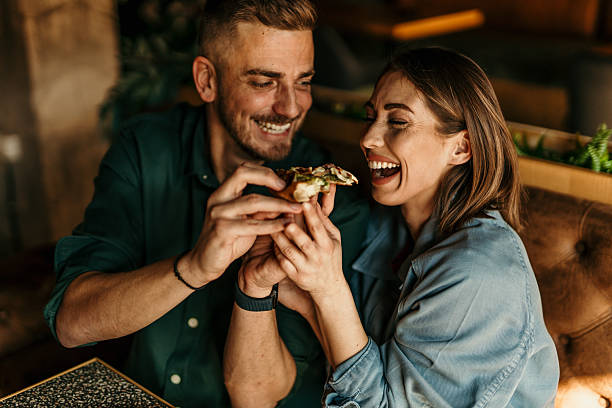 Couple sharing pizza slice, laughing and having fun at restaurant