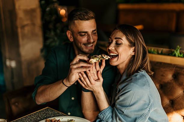 istock Young man feeding girlfriend with pizza slice in restaurant 2209673911