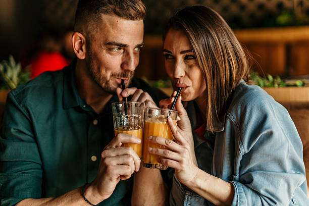 Young couple enjoying refreshing orange juice with straws in a cozy restaurant, gazing at each other with smiles and affection