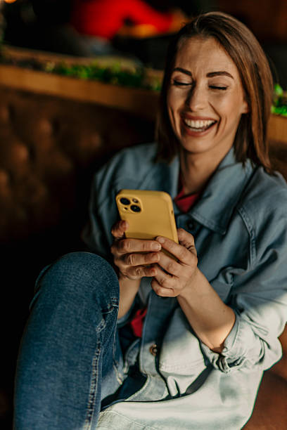 istock Young woman laughing while using mobile phone in a restaurant 2209674373