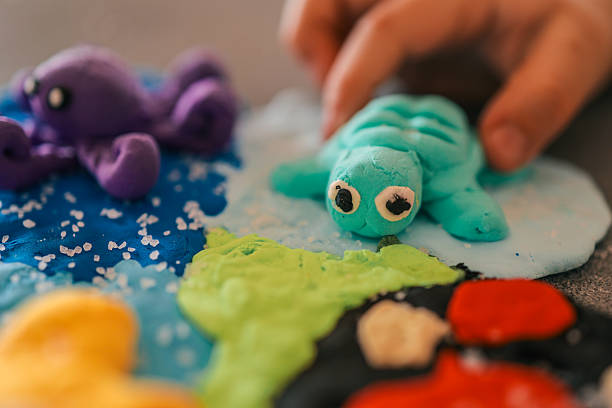 Colorful sea-themed scene made from modeling clay with a handmade turtle and octopus. A childâs hand plays with the turquoise turtle on a textured ocean base