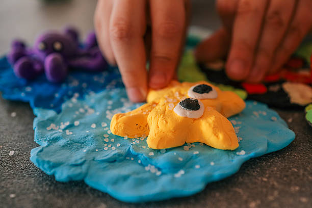 Child's hands playing with a handmade yellow starfish figure made from colorful modeling clay on a sea-themed background with textured details and salt crystals