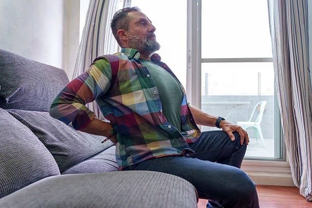istock Mature man suffering from back pain while sitting on sofa at home 2209678585