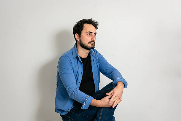 Man in blue shirt sitting against white wall