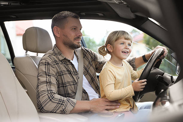 istock Man with his daughter holding steering wheel inside car 2209685454